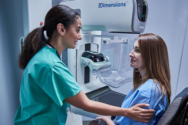 Une femme assise devant un mammographe avec un professionnel de santé à ses côtés