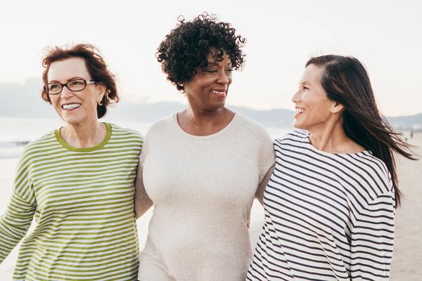 Trois femmes souriantes marchant ensemble sur une plage.