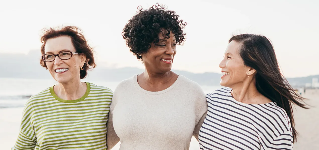 Trois femmes souriantes marchant ensemble sur une plage.