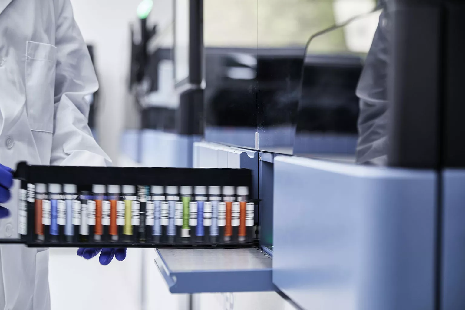 Une main gantée tient un rack de flacons dans un laboratoire.