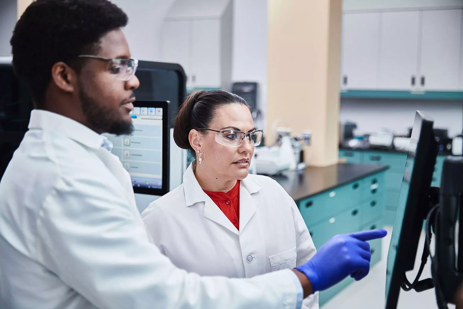 Technicien de laboratoire regardant et montrant du doigt un écran dans un laboratoire