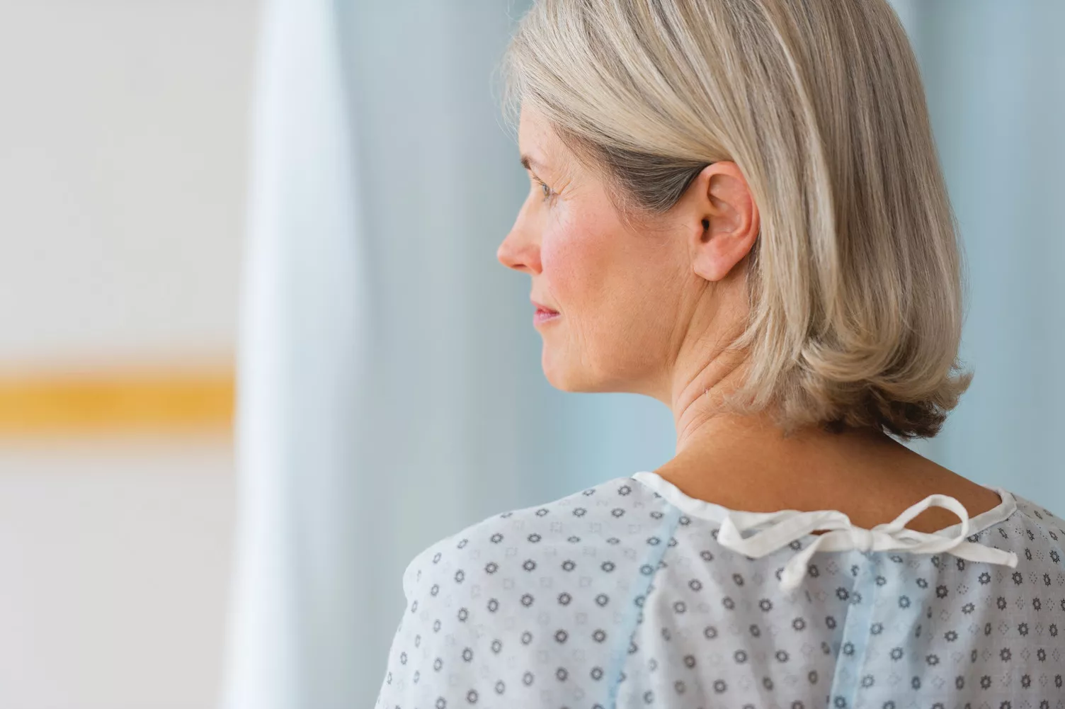 Femme âgée vêtue d’une blouse d’hôpital, regardant vers la gauche