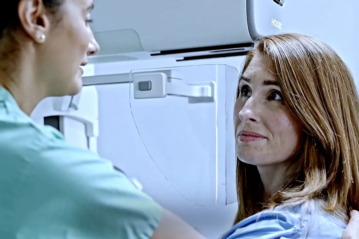 une femme à côté d'un équipement de dépistage du cancer du sein souriant à un professionnel de la santé